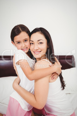 Portrait of happy mother hugging daughter on bed