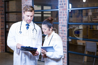 Two doctors looking at clipboard and discussing near library