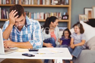 Tensed man by laptop while family sitting in background