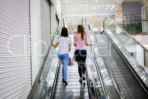 Rear view of two beautiful women on escalator of shopping mall