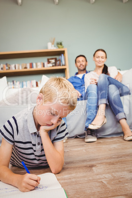 Boy drawing on book while parents looking at him