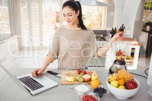Woman preparing fruit juice while working on laptop