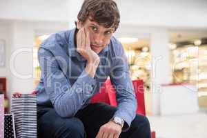 Man sitting in shopping mall with bored expression