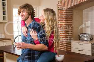 Cute couple cuddling with girlfriend sitting on the counter