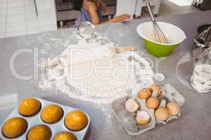 Rolling pin on dough with muffins and egg at kitchen table