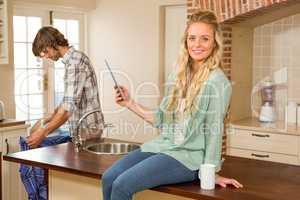 Pretty blonde using tablet while boyfriend ironing a shirt