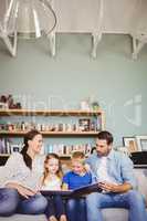 Smiling family reading book while sitting on sofa