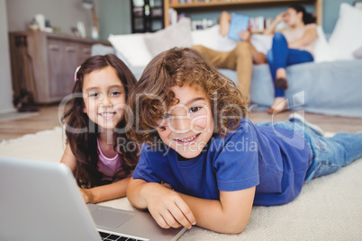 Portrait of siblings lying by laptop on carpet