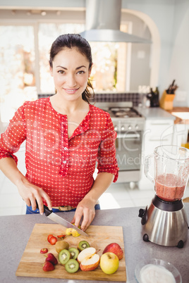 Portrait of smiling woman cutting fruits