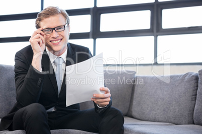 Happy young businessman holding document while sitting at sofa Happy young businessman holding document while sitting at sofa