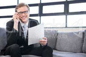 Happy young businessman holding document while sitting at sofa