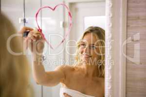 Beautiful blonde drawing big heart on mirror