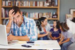 Tensed man by laptop table while family sitting in background