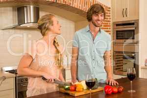 Cute couple enjoying a glass of wine and slicing vegetables