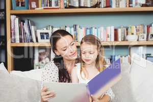 Mother and daughter reading book on sofa at home