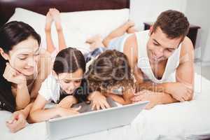 Happy children using laptop with parents on bed at home