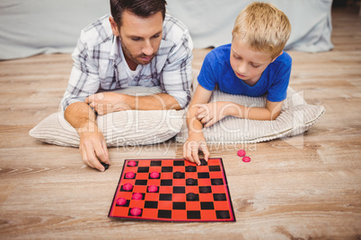 Father and son playing checker game while lying on hardwood floo