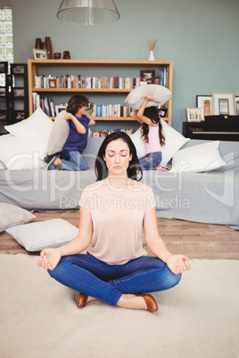 Woman meditating on carpet while children playing in background