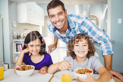 Happy man standing by children having breakfast