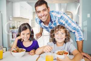 Happy man standing by children having breakfast