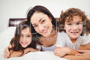 Cheerful woman with children lying on bed at home