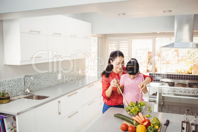 Smiling mother and daughter preparing vegetable salad