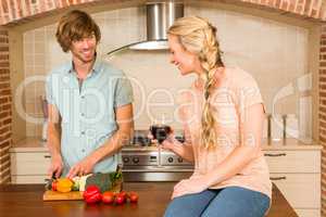 Cute couple enjoying a glass of wine and slicing vegetables