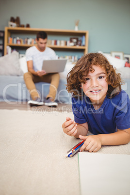 Portrait of boy lying on floor while father working in backgroun