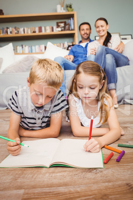 Children drawing on book while parents looking at them
