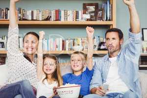 Cheerful family with arms raised while sitting on sofa