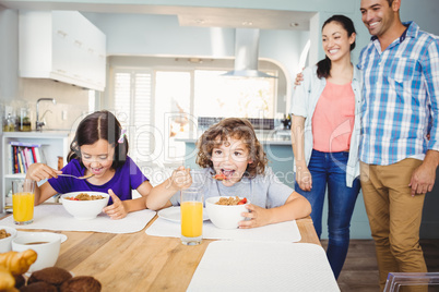 Children having breakfast while happy parents standing by table