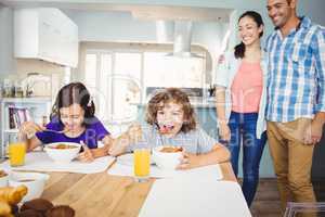 Children having breakfast while happy parents standing by table