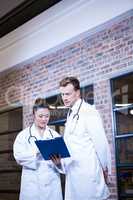 Two doctors looking at clipboard and discussing near library