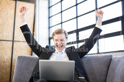 Businessman raising hands with excitement in front of laptop