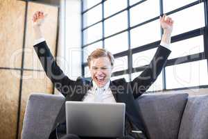 Businessman raising hands with excitement in front of laptop