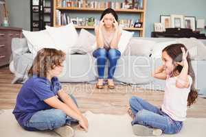Children playing while tensed mother sitting on sofa