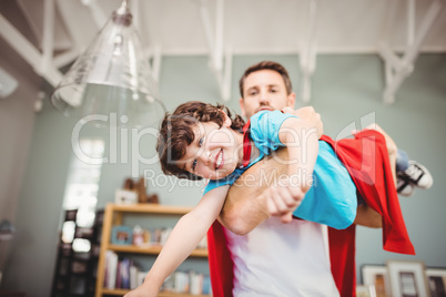 Portrait of father carrying son wearing superhero costume