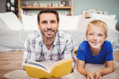 Father and son holding book lying on floor at home