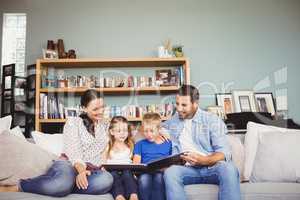 Happy family reading book while sitting on sofa