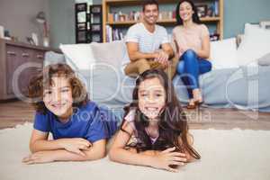 Siblings lying on carpet against parents siting on sofa