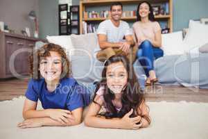 Son and daughter lying on carpet while parents sitting on sofa