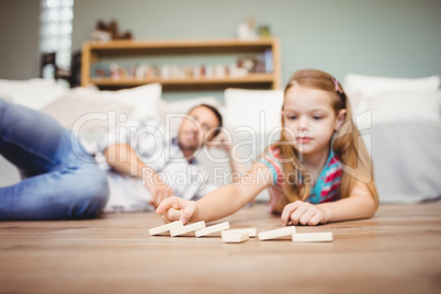 Girl arranging domino while father lying on hardwood floor at ho