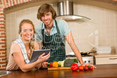 Cute couple slicing vegetables and using tablet