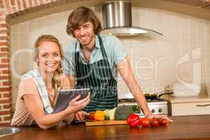 Cute couple slicing vegetables and using tablet