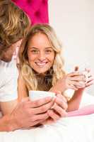 Cute couple relaxing on their bed and having coffee