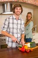 Handsome man slicing vegetables with girlfriend in background