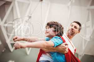 Low angle view of father holding cheerful son wearing superhero