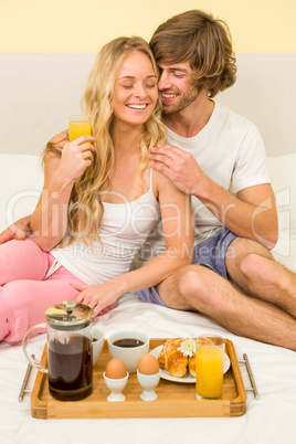 Cute couple having breakfast sitting on their bed