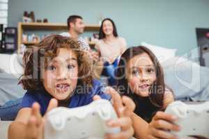 Cheerful siblings with controllers playing video game at home