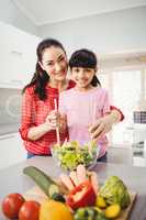 Portrait of smiling mother and daughter preparing vegetable sala